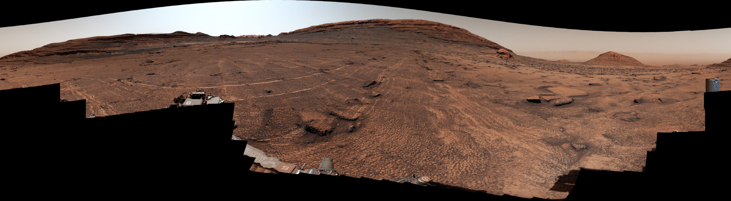 A sweeping Martian plain covered in honeycomb-like polygon fractures, leading toward distant hills, photographed by NASA's Curiosity rover